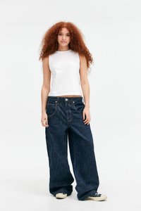 Jeans in denim scuro a gamba larga con accenti di cucitura visibili, abbinati a un top senza maniche aderente bianco. Il tessuto appare liscio e leggero.