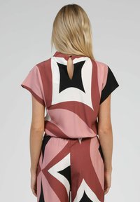 Combinaison multicolore avec des motifs géométriques dans des nuances de rose, noir et blanc. Ouverture en clé au dos. Texture de tissu lisse.
