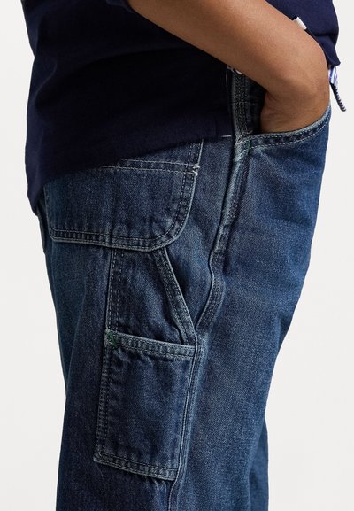 Calças cargo de denim azul-escuro com um bolso lateral, apresentando costura visível e um ajuste descontraído. Tecido texturizado com leve desvanecimento.