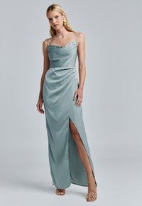 Satin-maksimekko vaalean teal-värissä, jossa on kaarroke, säädettävät hihnat, sivu-aukko ja rypytetty yksityiskohta, täydentävänä kultaisilla aksenteilla.