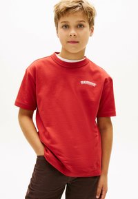 Rød bomulds T-shirt med rund halsudskæring og korte ærmer, prydet med et hvidt "TOMMY" logo broderet på venstre bryst.