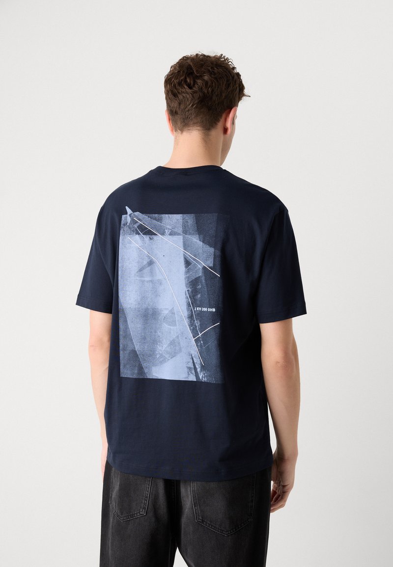 Camiseta de algodón azul marino de manga corta, con un gráfico geométrico en tonos azules en la parte posterior, que incluye acentos de líneas blancas y texto.