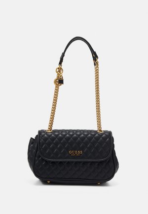 Sac à main noir matelassé Guess avec bandoulière chaîne dorée, plaque logo, et petit charm cadenas suspendu à la bandoulière sur fond blanc.