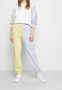 Survêtement en coloris blocs comprenant un sweat-shirt blanc, vert clair et bleu avec un col rond. Pantalons jaune pâle et bleu avec des poignets élastiques.