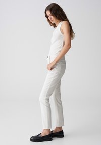 Canottiera bianca abbinata a jeans slim fit di colore chiaro e mocassini neri, caratterizzati da una silhouette dritta e da elementi di design minimi.