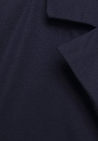 Tecido azul marinho com uma trama texturizada, apresentando seções de tecido sobrepostas que criam um efeito em camadas. Textura suave e macia.
