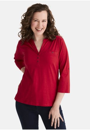 Rotes Oberteil mit drei Viertelärmeln, V-Ausschnitt und Knopfdetails. Verfügt über eine Brusttasche und einen weichen, strukturierten Stoff.