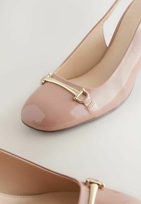 Pantofii slingback din piele patent roz deschis, cu vârful rotunjit și detaliu cu cataramă aurie în față, plasați pe un fundal neutru.