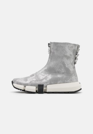 Botte baskets montantes argentée avec une fermeture éclair latérale, une semelle blanche segmentée, une semelle extérieure noire et un détail en métal en boucle à l'arrière du talon.