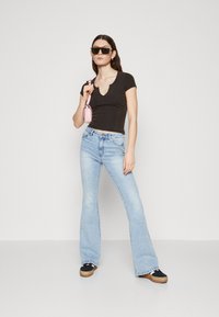Svart ribbestrikket topp med V-hals, lyseblå flared jeans og svarte sneakers med lys brun plattform. Rosa håndveske og mørke solbriller inkludert.