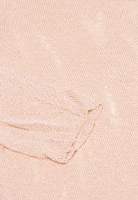 Maglione lavorato a maglia rosa chiaro con un motivo testurizzato. Presenta una manica ripiegata e dettagli leggermente a coste su tutto il tessuto.