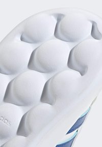 Suola della scarpa in bianco con rilievi arrotondati e testurizzati; presenta accenti blu e una finitura liscia. Branding visibile di lato.