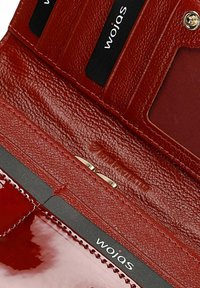 Portefeuille en cuir rouge avec plusieurs emplacements pour cartes, certains contenant des cartes noires marquées "wojas", et une fermeture à bouton pression.