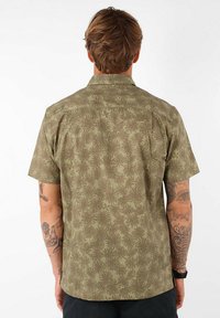 Chemise à manches courtes en vert olive avec un motif de feuilles, fabriquée en tissu léger, dotée d'un col et de détails au dos.
