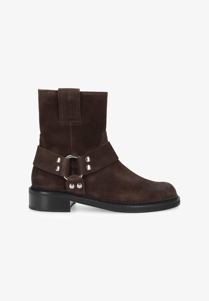 Bottine en daim marron avec un bout arrondi. Dotée d'une sangle et d'une boucle avec des accessoires en argent. Semelle en caoutchouc noire avec des accents cousus.