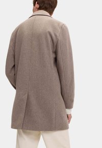 Abrigo de mezcla de lana marrón con una silueta entallada, abertura sencilla en la parte posterior y puños ligeramente acanalados, mostrado desde la espalda.