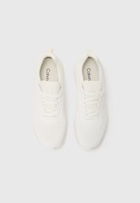 Zapatos deportivos blancos con parte superior de malla, diseño con cordones, collar acolchado y suela texturizada. Presenta un logo en la lengüeta y en la plantilla.