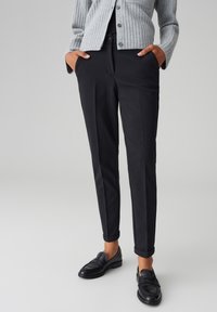 Pantaloni neri su misura con una vestibilità slim, tessuto liscio e risvolti, abbinati a un cardigan grigio a coste e mocassini neri.