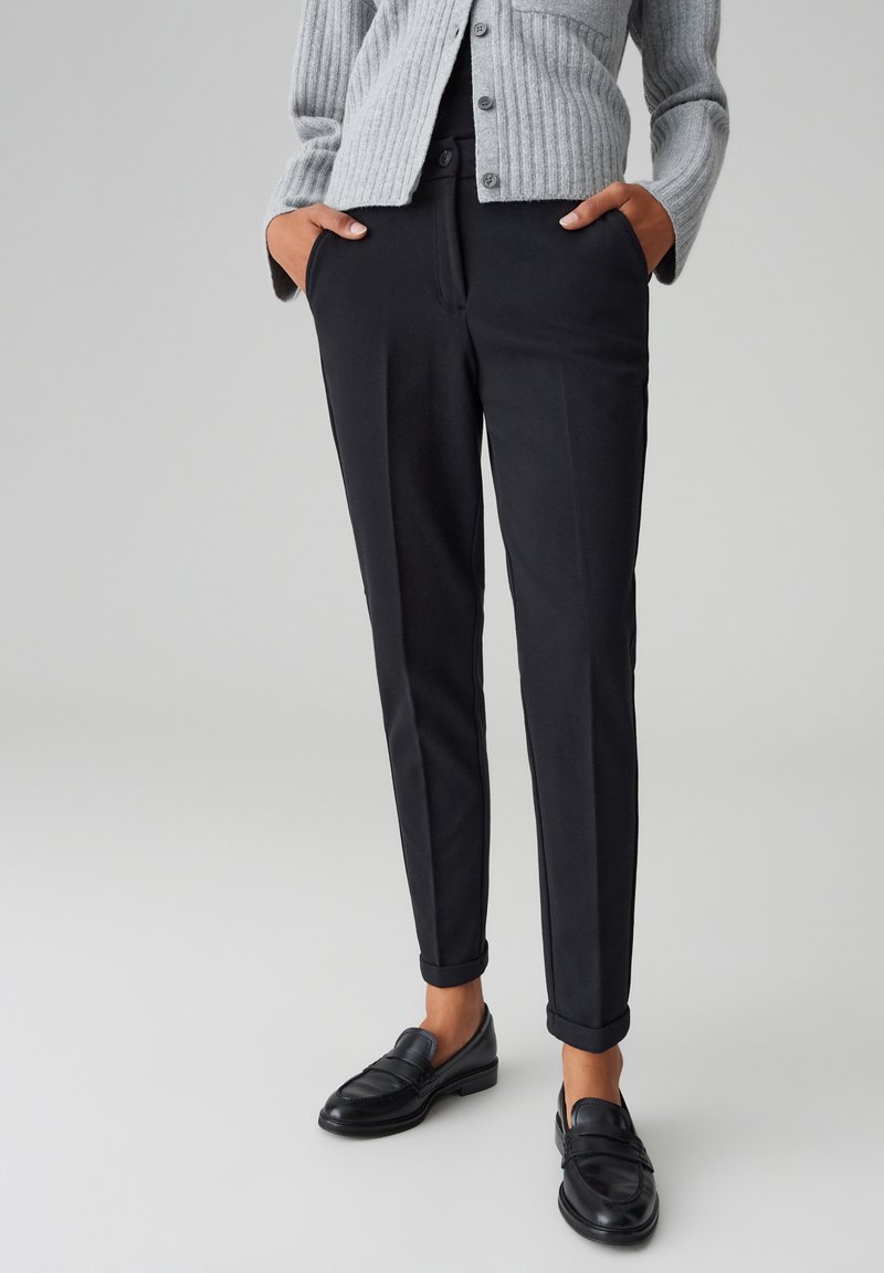 Pantaloni neri su misura con una vestibilità slim, tessuto liscio e risvolti, abbinati a un cardigan grigio a coste e mocassini neri.