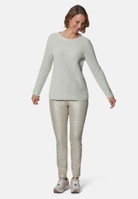 Lichtgroene gebreide trui met geribbelde textuur, ronde halslijn en lange mouwen, gecombineerd met glanzende beige broek en witte sneakers.