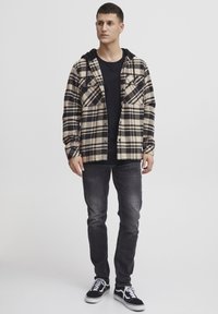 Koszula flanelowa w beżowo-czarną kratę, z dwoma kieszeniami na piersi. Nosi się ją na czarnej koszulce T-shirt i zestawia z ciemnymi dżinsami oraz czarnymi trampkami.