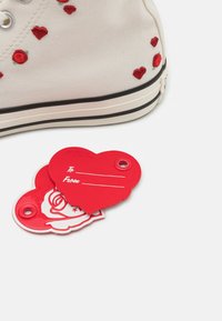 White canvas sneaker with red embroidered hearts, paired with red heart-shaped gift tags featuring "To" and "From" lines.