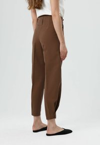 Bruine broek met een hoge taille, gemaakt van lichtgewicht stof, voorzien van zijzakken, taps toelopende pijpen en knoopdetails aan de manchetten.