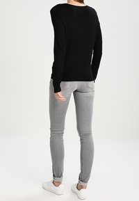 Svart långärmad tröja med rund halsringning, kombinerad med ljusgrå slim fit-jeans och vita snörskor. Slät textur, figurnära design.