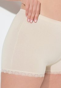 Boyshort in beige con bordo in pizzo, realizzati in tessuto morbido e liscio, con un design aderente e un delicato orlo in pizzo sulle gambe.