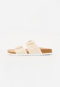 Beige sandaler med to justerbare stropper, laget av mykt stoff med gullfargede spenner, en kork såle og hvit gummisåle.