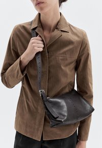 Borsa a tracolla in pelle nera con una finitura morbida e testurizzata, chiusura a zip e tracolla removibile. La borsa presenta dettagli di cucitura in evidenza.