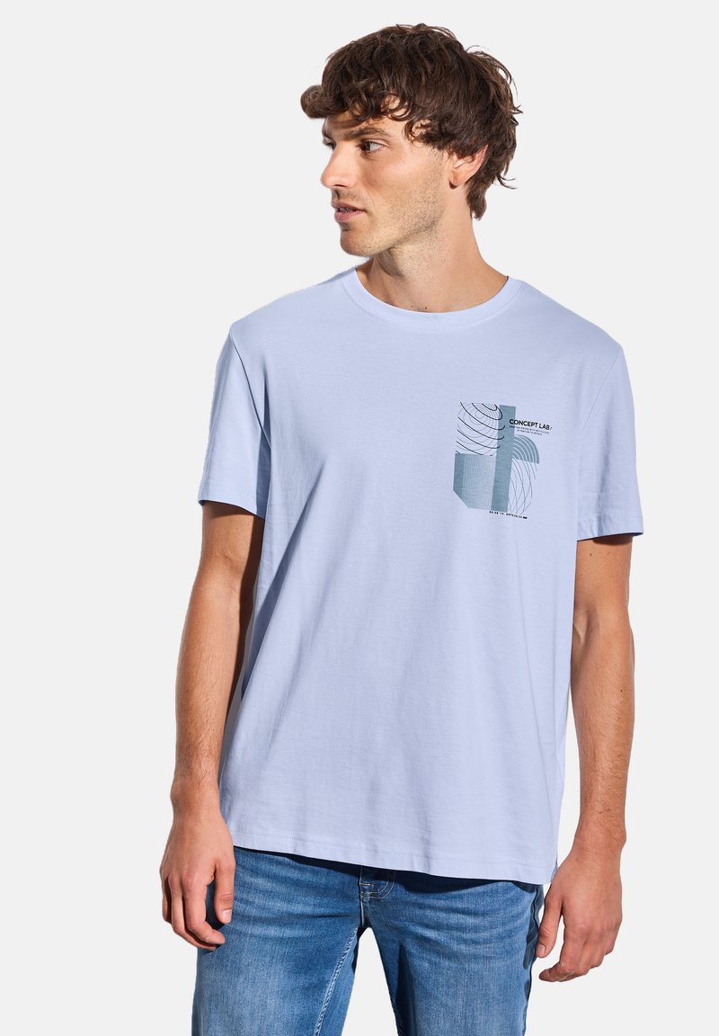 T-shirt en coton léger bleu clair avec un col rond et des manches courtes, présentant un motif graphique sur la poche imprimée en vert et noir.