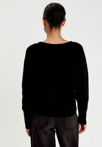 Schwarzer, gestrickter Pullover mit lockerer Passform, Rundhalsausschnitt und langen Ärmeln, kombiniert mit dunkelgrauen Jeans. Glatte Textur, schlichtes Design.