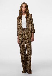 Conjunto de fato com padrão de pele de leopardo, composto por um blazer de corte solto e calças de perna larga, confeccionado em tecido macio em tons de castanho claro e castanho escuro.
