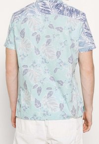 Koszula z krótkim rękawem w jasnym zielonym kolorze z różowymi i niebieskimi wzorami kwiatowymi. Posiada niebieski, wzorzysty karczek. Wykonana z lekkiego materiału.