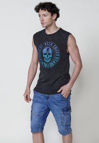 Svart ärmlös t-shirt med en blå och turkos dödskallegrafik, ihopparad med blå cargoshorts med sidofickor och en denimtextur.