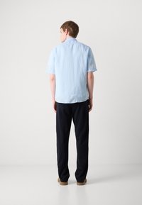Light blue short-sleeve shirt with a textured finish, paired with navy pants and brown shoes, viewed from the back against a plain background.
