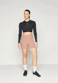 Conjunto atlético composto por uma blusa cropped preta de mangas longas ajustada e calções rosas de cintura alta. Os acessórios incluem meias brancas e sapatilhas pretas.