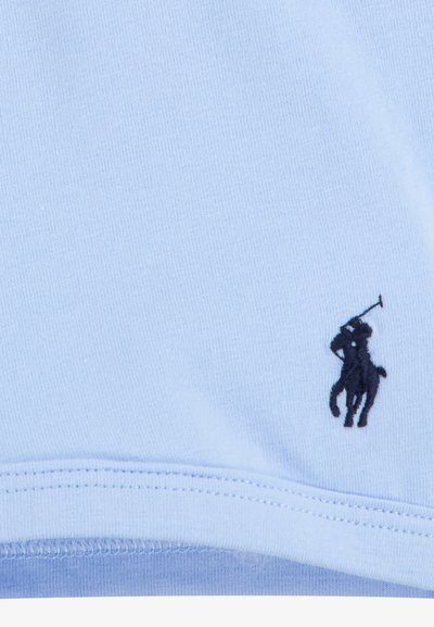 Svijetloplava pamuk tkanina s glatkom teksturom. Sadrži tamnoplavi izvezeni logo igrača polo blizu donjeg ruba. Jednostavan dizajn s klasičnim izgledom.