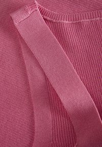 Rožinė megzta medžiaga su griovelių tekstūra. Nuotraukoje matoma diržo ir kaklo iškirpimo detalė, pabrėžianti minkštą medžiagą ir lygų siuvimą.