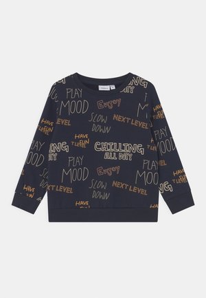 Sweat-shirt bleu marine à poignets élastiques, avec diverses phrases en beige et orange, dont "CHILLING ALL DAY" et "PLAY MOOD".