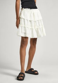 Gonna bianca a strati realizzata in tessuto leggero, con bordi arricciati e vita con coulisse. Indossata con sandali neri da infilare.