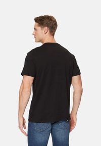 Camiseta negra de manga corta hecha de algodón, con cuello redondo y ajuste regular. Etiqueta visible en el dobladillo, combinada con jeans azules.
