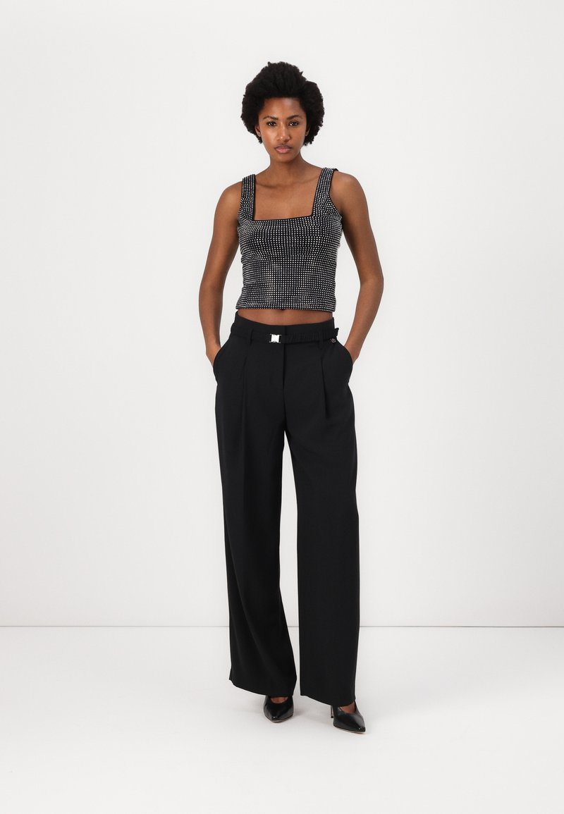 Schwarzes und weißes gemustertes Cropped-Top mit quadratischem Ausschnitt, kombiniert mit hoch taillierten schwarzen Hosen, die einen glänzenden Verschluss und Falten aufweisen.