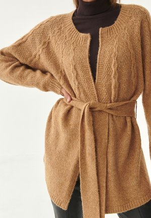 Cardigan en tricot camel avec un motif torsadé, devant ouvert et larges manches, resserré à la taille par une ceinture assortie.