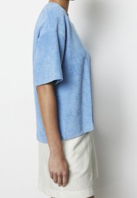 Blå t-shirt i frotté med korta ärmar, avslappnad passform, något oversized form och mjuk textur. Matchas med ljusfärgade shorts.