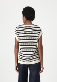 Strikket topp med marineblå og kremfargede horisontale striper, åpenhet detaljer, korte ermer og en avslappet passform. Teksturert ribbestrikket kant.