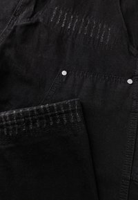 Zwart denim stof met een gestructureerd ontwerp, vervaagde accenten, koperen knoopdetails en een zichtbare zaknaad.