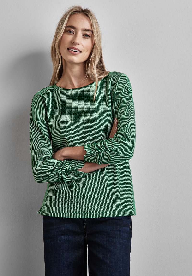 E groen gestreepte blouse met lange mouwen en een ronde halslijn, van een textuurstof en met geplooide manchetten. Draagt samen met donkere denim broek, op een effen achtergrond.