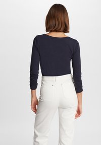 Langärmliges, marineblaues Oberteil kombiniert mit hochtaillierten weißen Jeans, die ein figurnahes Design und weichen Stoff aufweisen, sichtbare Rückennähte und einfache Nähte.